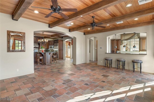 unfurnished living room with beamed ceiling, ceiling fan with notable chandelier, dark tile patterned floors, and wooden ceiling