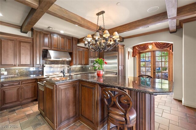 kitchen with beam ceiling, tasteful backsplash, a center island with sink, tile patterned floors, and built in appliances