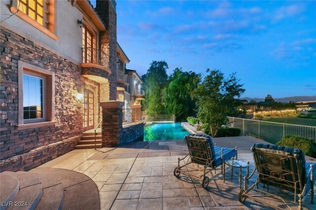 patio terrace at dusk featuring a fenced in pool