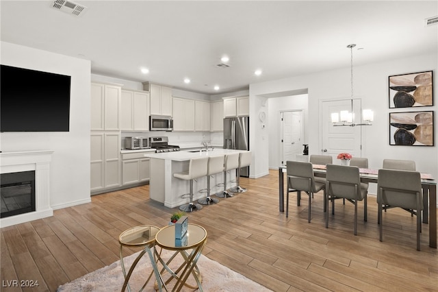 kitchen featuring a notable chandelier, appliances with stainless steel finishes, an island with sink, light hardwood / wood-style floors, and white cabinets