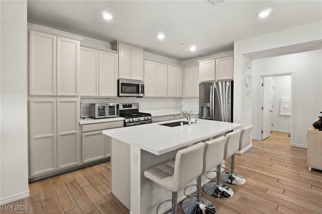 kitchen with sink, stainless steel appliances, a kitchen island with sink, and light hardwood / wood-style flooring