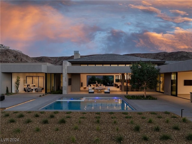 pool at dusk with an outdoor living space, a mountain view, and a patio area