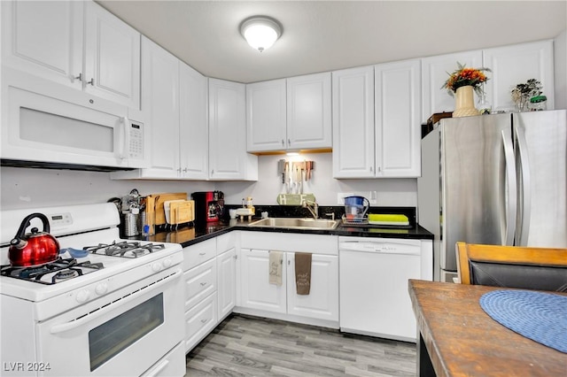 kitchen featuring white appliances, a sink, white cabinetry, light wood finished floors, and dark countertops