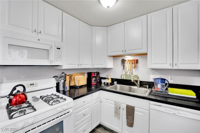 kitchen featuring white appliances, dark countertops, a sink, and white cabinetry