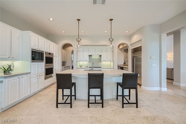 kitchen featuring backsplash, hanging light fixtures, white cabinets, light tile patterned floors, and a center island with sink