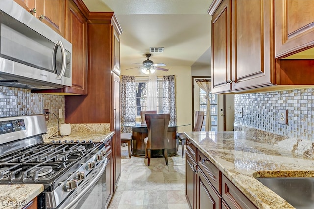 kitchen with ceiling fan, tasteful backsplash, light stone countertops, light tile patterned flooring, and stainless steel appliances