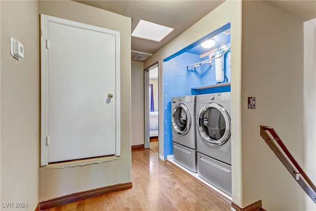 laundry room featuring laundry area, washer and clothes dryer, a skylight, and light wood-style flooring