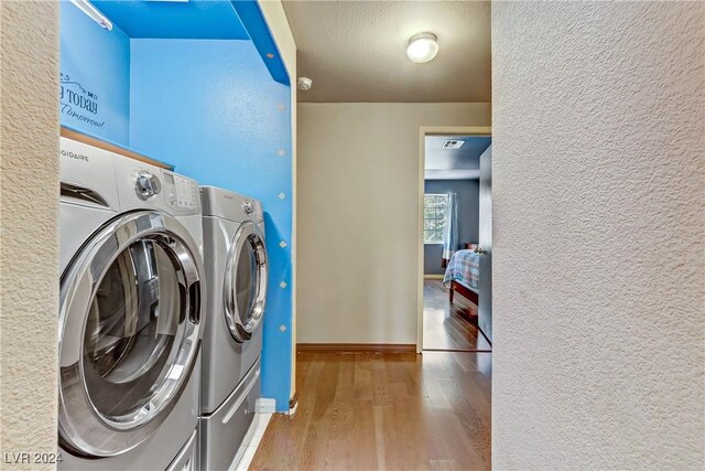 clothes washing area with washing machine and dryer and light hardwood / wood-style flooring