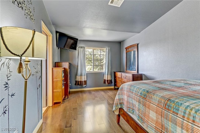 bedroom featuring a textured ceiling, a textured wall, visible vents, baseboards, and light wood finished floors