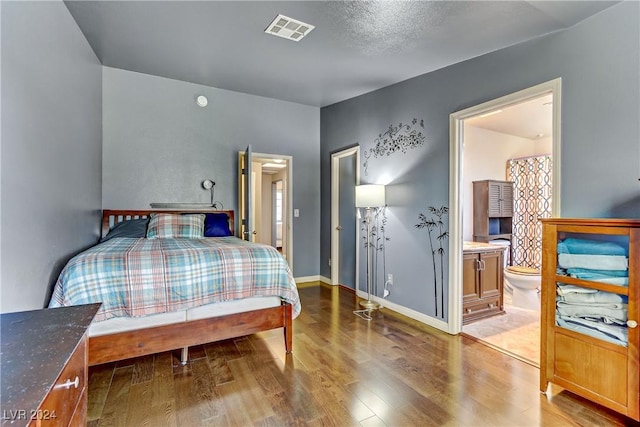 bedroom with baseboards, connected bathroom, visible vents, and wood finished floors