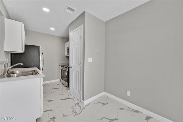 kitchen featuring sink, range, refrigerator, and white cabinetry