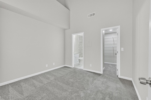 unfurnished bedroom featuring high vaulted ceiling, a closet, a spacious closet, connected bathroom, and carpet flooring