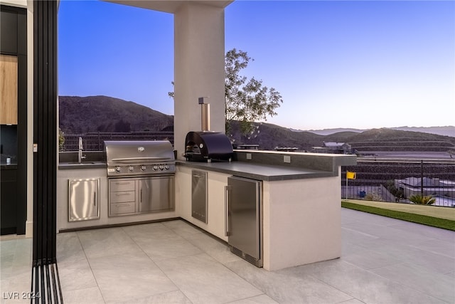 patio terrace at dusk with exterior kitchen, a mountain view, sink, and a grill