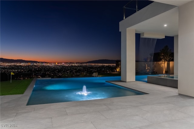 pool at dusk featuring pool water feature and a patio