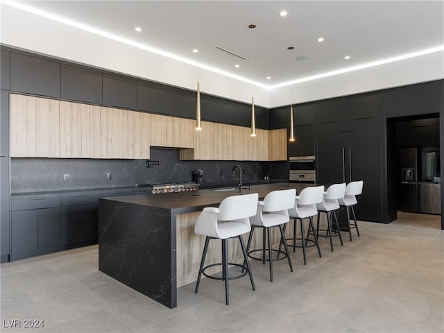 kitchen with light brown cabinets, a kitchen breakfast bar, pendant lighting, tasteful backsplash, and a center island with sink