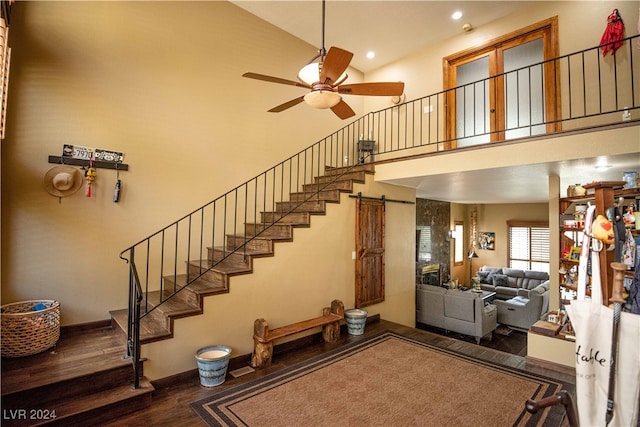 stairs with ceiling fan, high vaulted ceiling, wood-type flooring, and a barn door