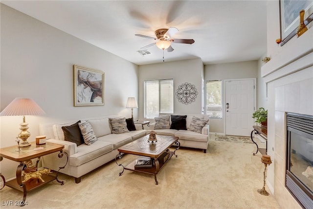 living room with ceiling fan, a tiled fireplace, and light carpet