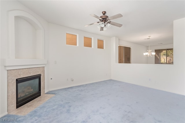 unfurnished living room with carpet floors, a tiled fireplace, and ceiling fan with notable chandelier