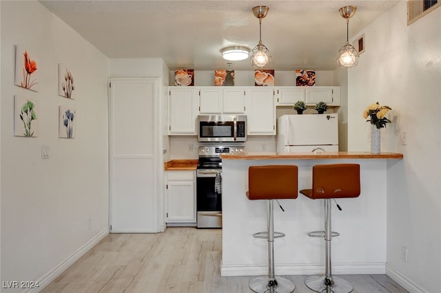 kitchen featuring appliances with stainless steel finishes, white cabinetry, a kitchen bar, light wood-type flooring, and hanging light fixtures