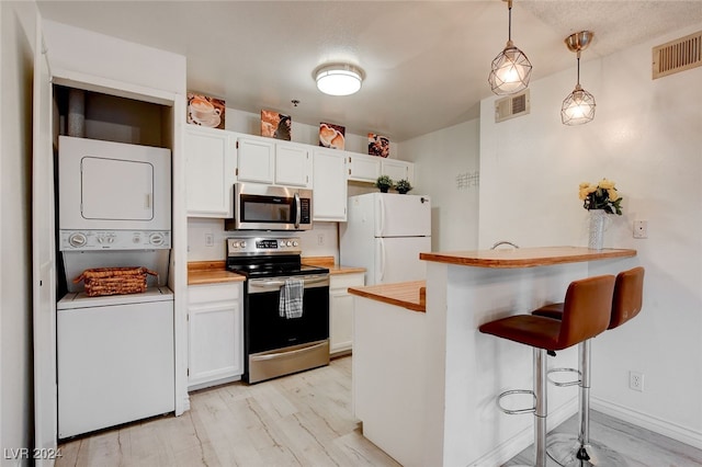 kitchen with white cabinets, light hardwood / wood-style flooring, appliances with stainless steel finishes, and stacked washer and clothes dryer