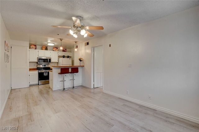 kitchen with appliances with stainless steel finishes, light hardwood / wood-style floors, white cabinets, kitchen peninsula, and a breakfast bar area