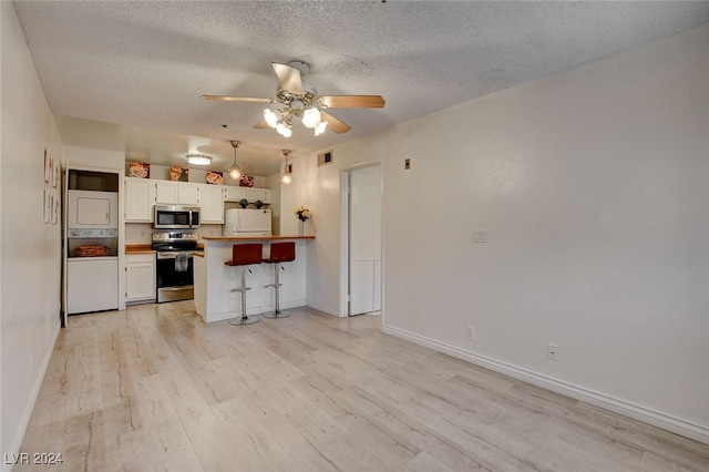 kitchen featuring appliances with stainless steel finishes, light hardwood / wood-style floors, white cabinets, kitchen peninsula, and a breakfast bar