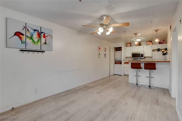 kitchen featuring a kitchen bar, light wood-type flooring, a textured ceiling, white cabinets, and white refrigerator