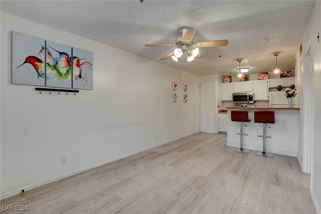 unfurnished living room featuring ceiling fan, light hardwood / wood-style flooring, and a textured ceiling