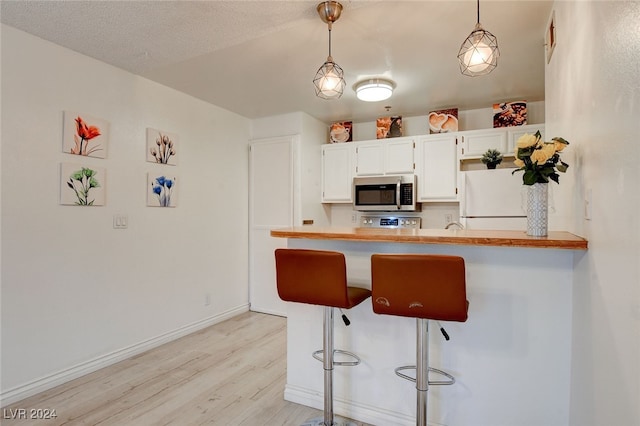 kitchen with a breakfast bar, decorative light fixtures, white fridge, light hardwood / wood-style floors, and white cabinets