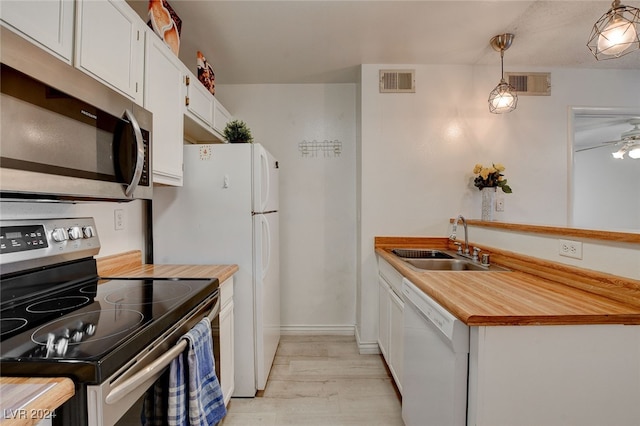 kitchen with sink, light wood-type flooring, appliances with stainless steel finishes, white cabinetry, and hanging light fixtures