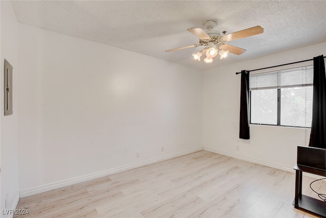 empty room with a textured ceiling, light hardwood / wood-style flooring, ceiling fan, and electric panel