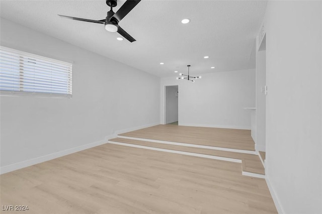 unfurnished living room with ceiling fan with notable chandelier, a textured ceiling, and light wood-type flooring