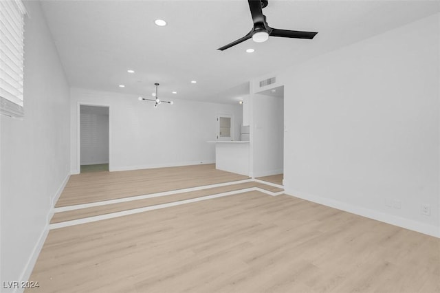 unfurnished living room with ceiling fan with notable chandelier and light wood-type flooring