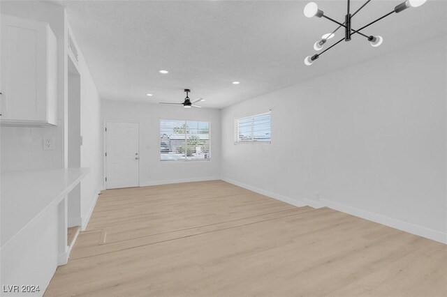 unfurnished room with ceiling fan with notable chandelier and light hardwood / wood-style floors