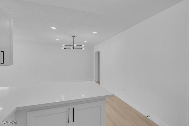 interior space featuring pendant lighting, light hardwood / wood-style flooring, a chandelier, and white cabinets