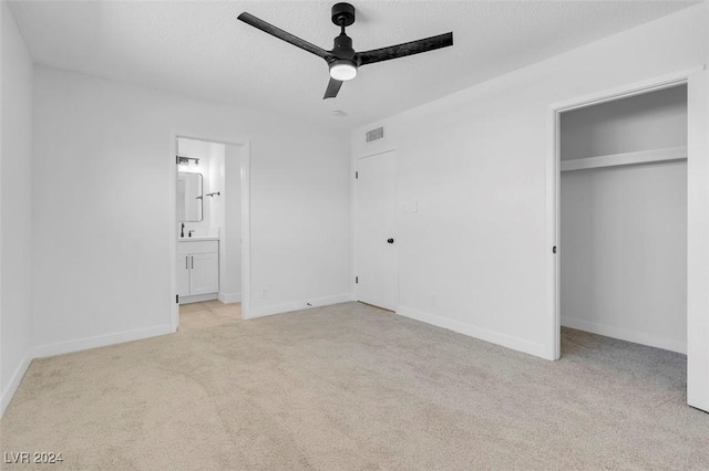 unfurnished bedroom featuring ensuite bath, ceiling fan, a textured ceiling, light carpet, and a closet