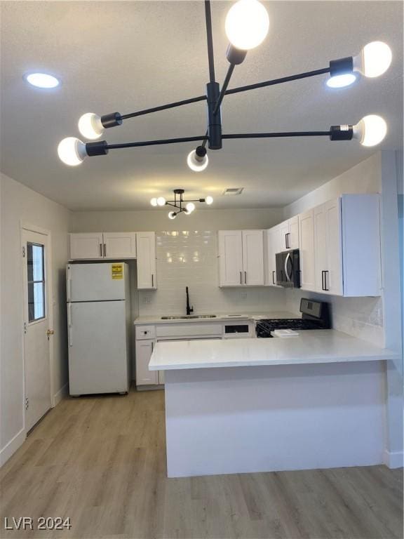 kitchen featuring white refrigerator, white cabinets, kitchen peninsula, and stove