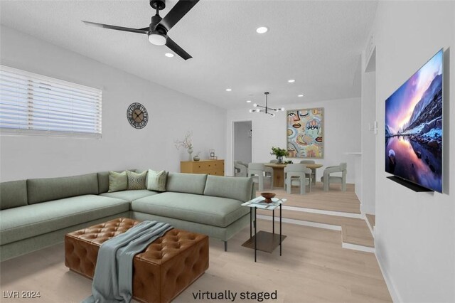 living room featuring ceiling fan with notable chandelier, light hardwood / wood-style floors, and a textured ceiling