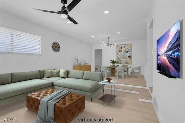 living room featuring ceiling fan with notable chandelier, light hardwood / wood-style flooring, and a textured ceiling