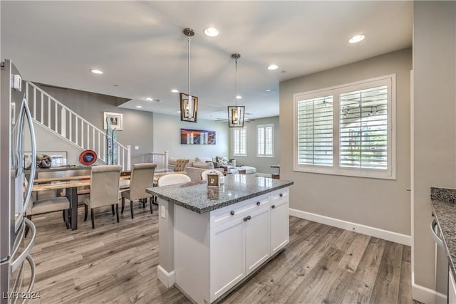 kitchen featuring dark stone counters, light hardwood / wood-style flooring, decorative light fixtures, white cabinetry, and stainless steel refrigerator