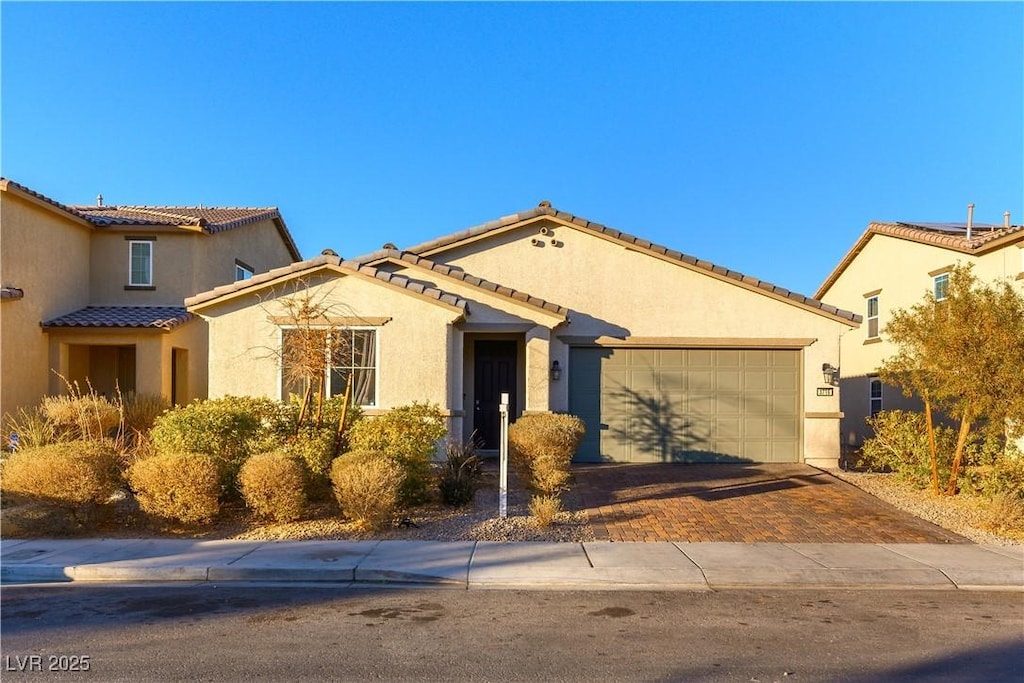 view of front of house featuring stucco siding, a tiled roof, driveway, and a garage