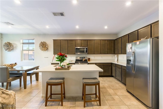 kitchen featuring dark brown cabinets, stainless steel appliances, a kitchen bar, and a kitchen island