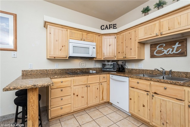 kitchen featuring sink, white appliances, light brown cabinetry, light tile patterned floors, and a breakfast bar area