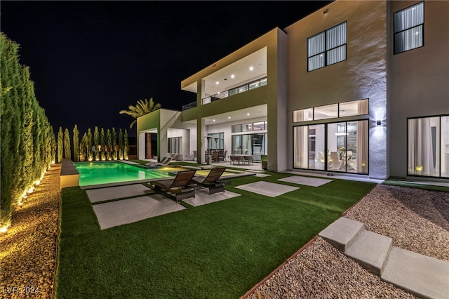 back of house at twilight featuring a patio, an outdoor pool, a balcony, and stucco siding