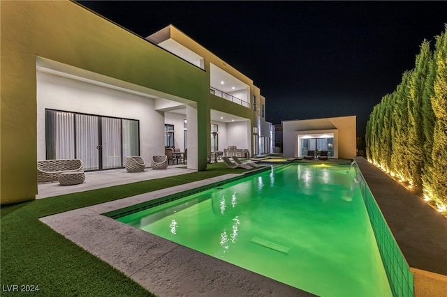 pool at night featuring a patio area and an outdoor pool