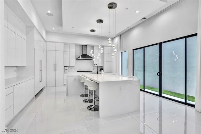 kitchen featuring wall chimney range hood, modern cabinets, white cabinetry, and a kitchen breakfast bar