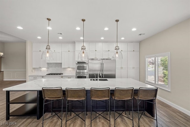 kitchen with a kitchen breakfast bar, light stone countertops, a large island with sink, and appliances with stainless steel finishes