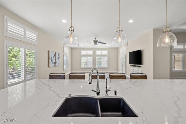 kitchen with pendant lighting, light stone counters, ceiling fan, and sink