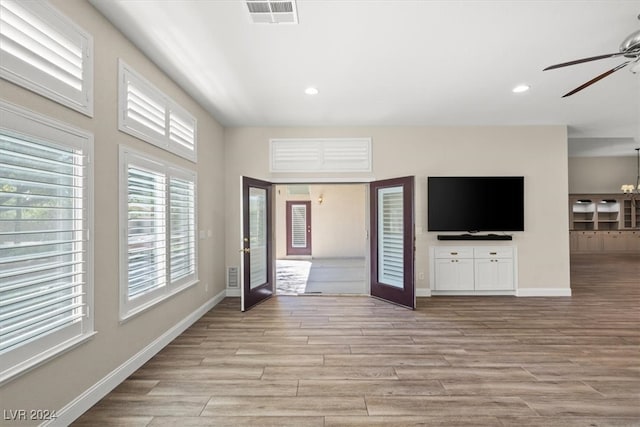 unfurnished living room featuring light hardwood / wood-style flooring, ceiling fan with notable chandelier, and french doors