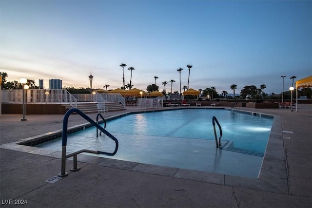 pool at dusk featuring a patio area and a community pool